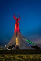 Ouzbékistan, Tachkent - mai 5, 2023 illuminé monument de indépendance dans le forme de une stèle avec une humo oiseau, fontaines et agitant drapeaux dans le Nouveau Ouzbékistan parc à la nuit. photo