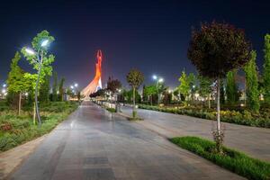 Ouzbékistan, Tachkent - mai 5, 2023 illuminé monument de indépendance dans le forme de une stèle avec une humo oiseau, fontaines et agitant drapeaux dans le Nouveau Ouzbékistan parc à la nuit. photo