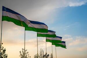 drapeaux de Ouzbékistan agitant sur une le coucher du soleil ou lever du soleil spectaculaire ciel Contexte. photo