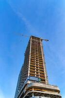 une grue bâtiment une gratte-ciel contre une bleu ciel. photo