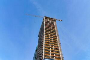 une grue bâtiment une gratte-ciel contre une bleu ciel. photo