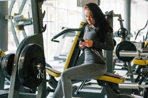 magnifique Jeune femme envoyer des SMS et social la mise en réseau tandis que dans une salle de sport. photo