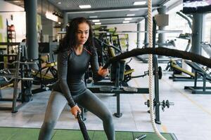 aptitude sur le Cordes. magnifique femelle dans Gym travail en dehors avec corde. Jeune femme formation difficile photo