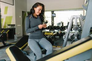 magnifique Jeune femme envoyer des SMS et social la mise en réseau tandis que dans une salle de sport. photo