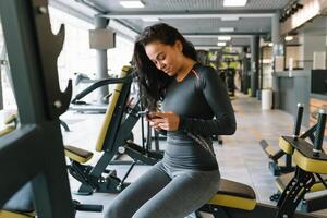 magnifique Jeune femme envoyer des SMS et social la mise en réseau tandis que dans une salle de sport. photo