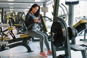 magnifique Jeune femme envoyer des SMS et social la mise en réseau tandis que dans une salle de sport. photo