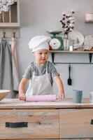 Jeune garçon mignonne sur le cuisine cuisinier chef dans blanc uniforme et chapeau près tableau. fait maison pain d'épice. le garçon cuit le Chocolat biscuits photo