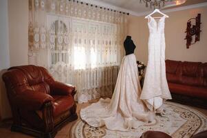 magnifique de la mariée blanc mariage robe bloque près le lit dans une Hôtel pièce avec fleurs à le bas. de mariée Matin avant la cérémonie photo