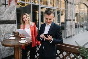 Beau et sur de soi homme d'affaire en utilisant portable ordinateur et La technologie gadget téléphone intelligent Extérieur discuter avec magnifique affaires partenaire .nouveau moderne affaires gens mode de vie photo