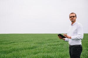 Jeune agronome détient tablette toucher tampon ordinateur dans vert blé champ. secteur agroalimentaire concept. agricole ingénieur permanent dans une blé champ avec une tablette dans été photo