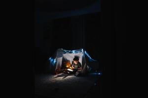 enfant garçon en train de lire avec livre et lampe de poche et nounours ours dans tente. avant Aller à lit. photo