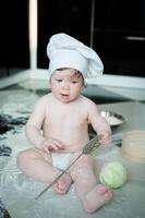 peu garçon séance sur tapis dans cuisine en jouant avec cuisine marmites. mignonne garçon cuisine dans cuisine à Accueil photo