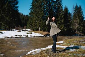 femme dans une chapeau et vert veste est repos sur le la nature dans le montagnes près le Montagne rivière. se détendre temps sur vacances concept Voyage. photo