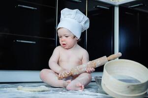 peu garçon séance sur tapis dans cuisine en jouant avec cuisine marmites. mignonne garçon cuisine dans cuisine à Accueil photo