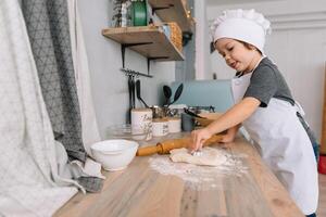 Jeune garçon mignonne sur le cuisine cuisinier chef dans blanc uniforme et chapeau près tableau. Noël fait maison pain d'épice. le garçon cuit le Chocolat biscuits. photo