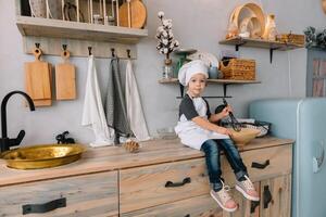 Jeune garçon mignonne sur le cuisine cuisinier chef dans blanc uniforme et chapeau près tableau. Noël fait maison pain d'épice. le garçon cuit le Chocolat biscuits. photo