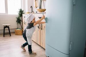 Jeune content maman et sa bébé cuisinier biscuits à Accueil dans le cuisine. Noël fait maison pain d'épice. mignonne garçon avec mère dans blanc uniforme et chapeau cuit Chocolat biscuits. photo