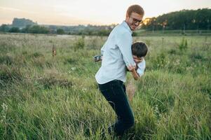 Beau papa avec le sien peu mignonne fils sont ayant amusement et en jouant sur vert herbeux pelouse. content famille concept. beauté la nature scène avec famille Extérieur mode de vie. famille repos ensemble. les pères journée. photo