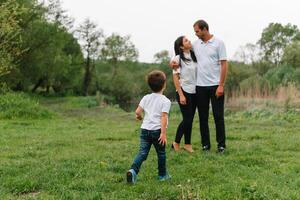 content famille mère père et enfant fils sur la nature sur le coucher du soleil. maman, papa et enfant en riant et étreindre, profiter la nature dehors. ensoleillé jour, bien ambiance. concept de une content famille. photo