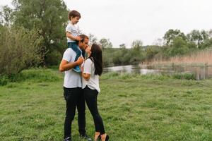 content famille mère père et enfant fils sur la nature sur le coucher du soleil. maman, papa et enfant en riant et étreindre, profiter la nature dehors. ensoleillé jour, bien ambiance. concept de une content famille. photo