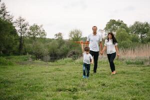 père, mère et fils en jouant avec jouet avion dans le parc. amical famille. gens ayant amusement en plein air. image fabriqué sur le Contexte de le parc et bleu ciel. concept de une content famille photo