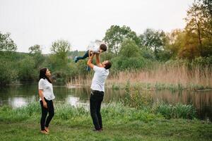 content famille mère père et enfant fils sur la nature sur le coucher du soleil. maman, papa et enfant en riant et étreindre, profiter la nature dehors. ensoleillé jour, bien ambiance. concept de une content famille. photo