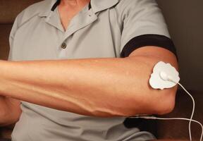 homme en utilisant un électro thérapie masseur ou dizaines unité sur le sien coude pour douleur le soulagement de muscles et mixte photo