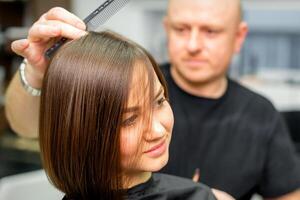 Jeune caucasien brunette femme ayant sa coiffure par une Masculin coiffeur à une parloir. photo