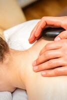 chaud pierre massage thérapie. caucasien Jeune femme avoir une chaud pierre massage sur retour à spa salon. photo