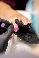 La peinture ongles de une femme. mains de manucure dans noir gants appliquant rose clou polonais sur femelle ongles dans une beauté salon. photo