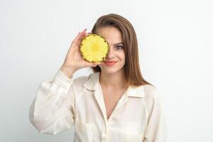 attrayant jolie agréable Jeune caucasien femme tenir tranché ananas couvrant sa œil isolé sur blanc Couleur Contexte. photo