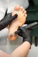 peeling femelle pieds. mains de podologie spécialiste dans noir gants en utilisant spécial broyage équipement polonais femelle pied de cal et blé dans le beauté salon. photo