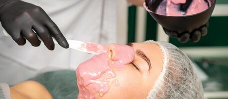 le cosmétologue appliquant un alginate masque à le visage de une Jeune femme dans une beauté salon. photo