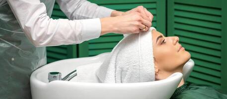une coiffeur est emballage une femelle tête dans une serviette après la lessive cheveux dans le beauté salon. photo