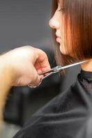 femme ayant une Nouveau la Coupe de cheveux. Masculin coiffeur Coupe marron cheveux avec les ciseaux dans une cheveux salon. photo