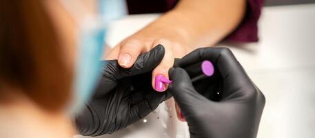 La peinture ongles de une femme. mains de manucure dans noir gants appliquant rose clou polonais sur femelle ongles dans une beauté salon. photo