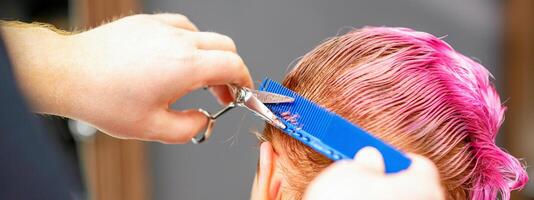 professionnel coiffeur est Coupe court rose cheveux avec les ciseaux dans cheveux salon proche en haut. photo
