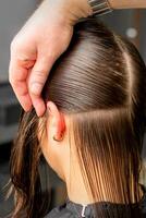 coiffeur divise femelle cheveux dans sections avec peigne en portant cheveux avec sa mains dans cheveux salon proche en haut. photo