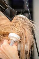 coiffeur main séchage blond cheveux avec une sèche-cheveux et rond brosse dans une beauté salon. photo