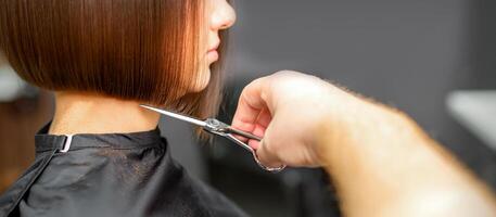 femme ayant une Nouveau la Coupe de cheveux. Masculin coiffeur Coupe marron cheveux avec les ciseaux dans une cheveux salon. photo