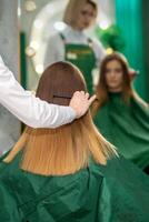 une femelle coiffeur est ratissage le longue marron cheveux de une Jeune femme à une parloir. photo