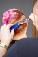 femme ayant une Nouveau la Coupe de cheveux. Masculin coiffeur Coupe rose court cheveux avec les ciseaux dans une cheveux salon. photo