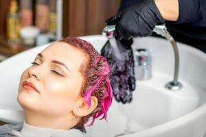 la lessive teint femelle cheveux. professionnel coiffeur lavages rose Couleur peindre de de une client. Jeune caucasien femme ayant sa cheveux lavé dans une beauté salon. photo