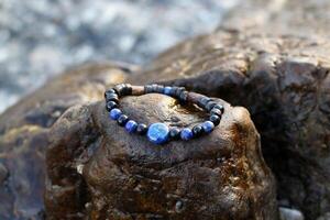 bracelet fabriqué de Naturel matériaux - noir agate, bleu lazurite et en bois éléments sur une humide pierre près à mer. artisanat précieux article. bijoux accessoires. photo