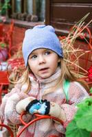 une Jeune femme dans une bleu chapeau admire une vibrant rouge fleur dans une jardin rempli avec coloré fleurit. elle porte une blanc et gris veste cette compléments sa blond cheveux, lequel brille dans le lumière du soleil. photo