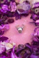 argent bague avec rose pierre sur une rose Contexte avec sec violet fleurs. artisanat précieux article. bijoux accessoires. photo