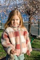 Jeune fille profiter une ensoleillé journée près une épanouissement arbre avec magnifique blanc fleurs dans une parc. photo