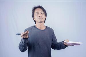 Beau asiatique homme est montrer du doigt à un vide assiette avec une sombre expression, isolé blanc Contexte pour La publicité photocopie. photo