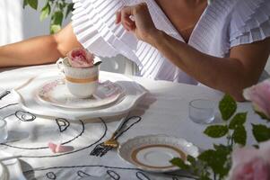 une femme, une fille dans une blanc robe est assis à une table et détient une tasse de thé ou café dans sa mains. avoir certains thé. Matin de le la mariée. photo