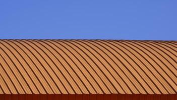 courbe ligne modèle de Orange ondulé acier incurvé toit contre bleu clair ciel Contexte photo